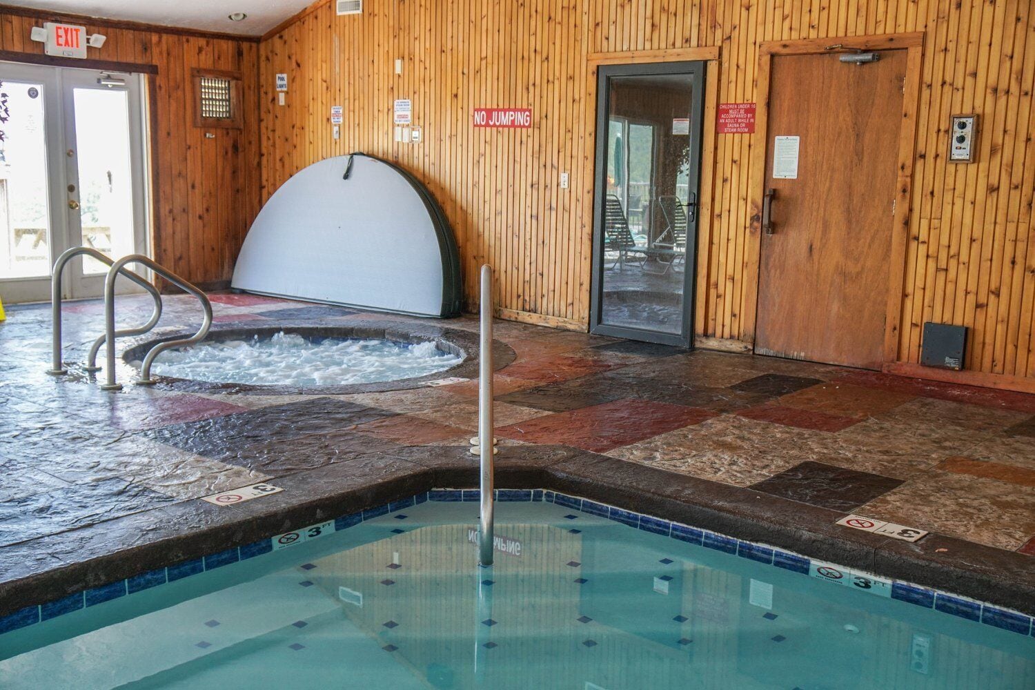 An indoor swimming pool with a hot tub, wooden walls, and a tiled floor.