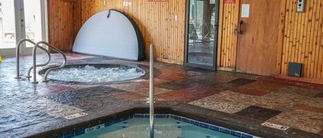 An indoor swimming pool with a hot tub, wooden walls, and a tiled floor.