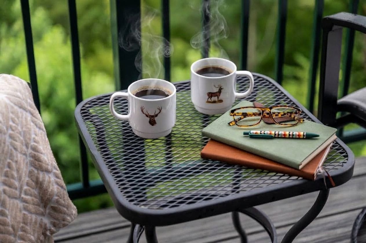 Een metalen tafel met twee koffiekopjes, een bril, een notitieboekje en een pen.