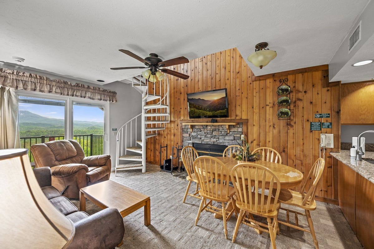 Ein gemütliches Wohnzimmer mit Kamin, Holzwänden, einem Essbereich und einer Treppe, die zu einem Balkon führt.