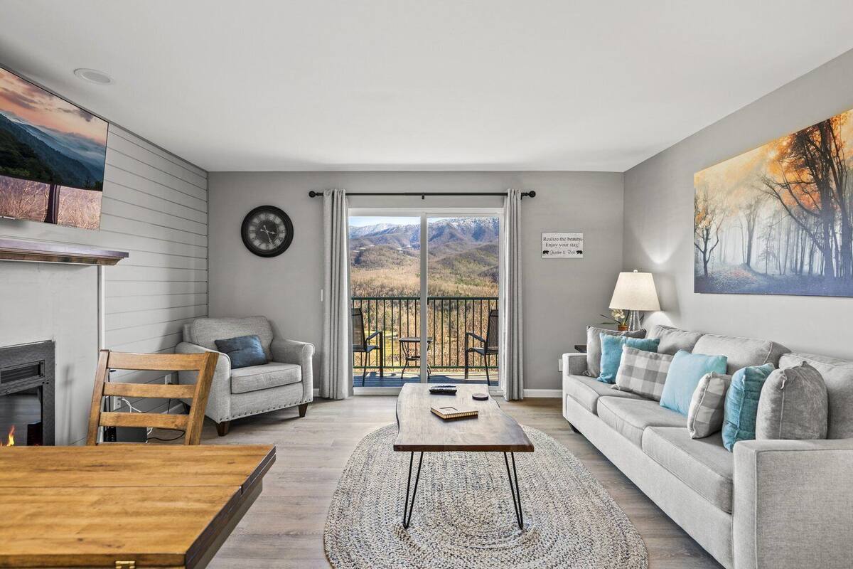 Ein modernes Wohnzimmer mit Kamin, Essbereich und einem Balkon mit Bergblick.