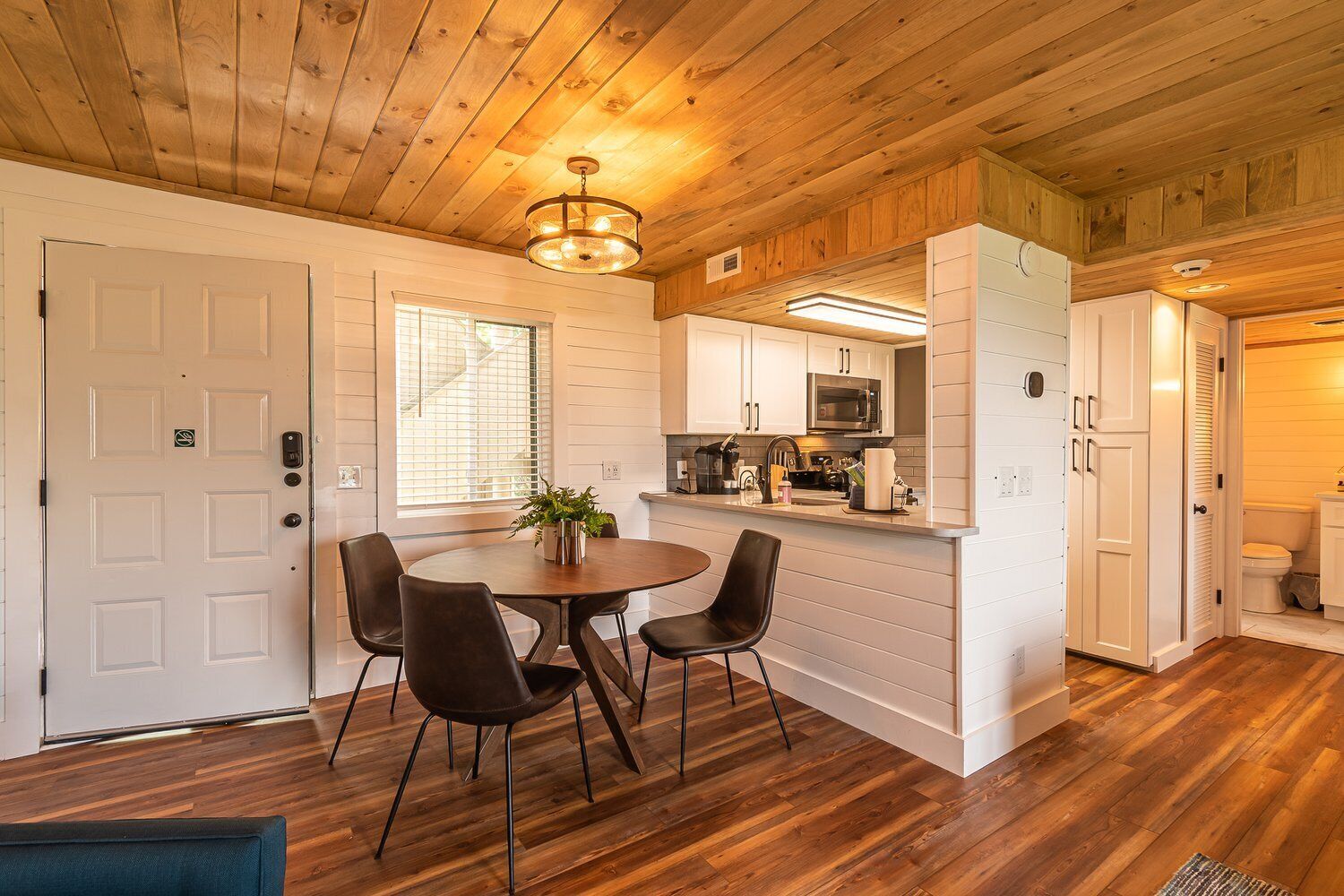 A modern kitchen with white cabinets, a microwave, and a sink. There is a dining area with a round table and chairs.