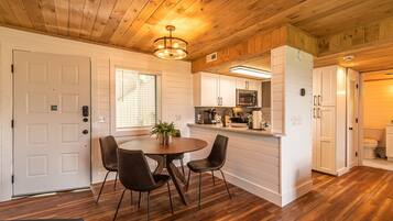 A modern kitchen with white cabinets, a microwave, and a sink. There is a dining area with a round table and chairs.