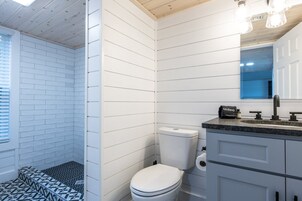 Ein Badezimmer mit weißen Fliesen, einer weißen Toilette, einem schwarz-weißen Duschboden und einem modernen Waschbecken mit Spiegel darüber.