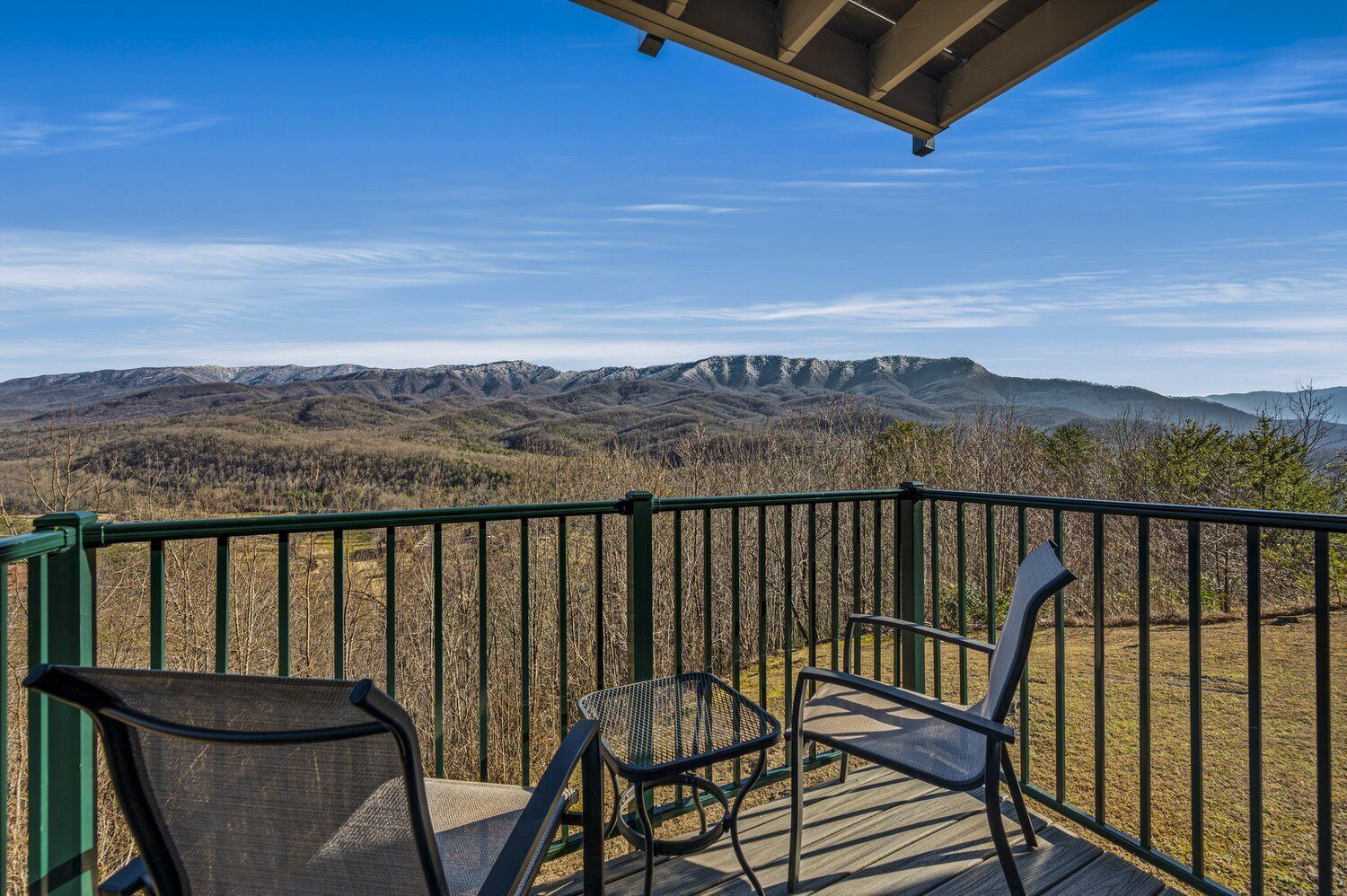 A balcony with a view of mountains, a covered area, and two chairs.