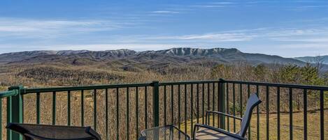 A balcony with a view of mountains, a covered area, and two chairs.