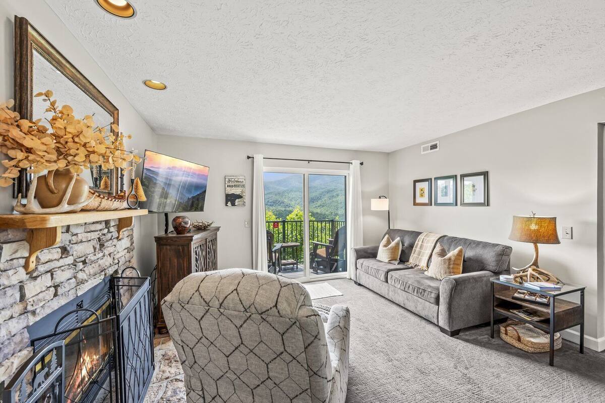 Ein gemütliches Wohnzimmer mit Kamin, einer Couch, einem Sessel und einem Balkon mit Panoramablick.