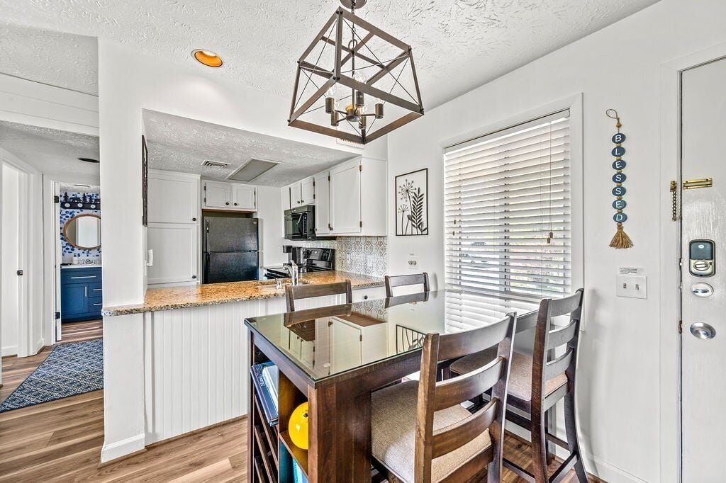A modern kitchen with white cabinets, a granite countertop, and a hanging light fixture.
