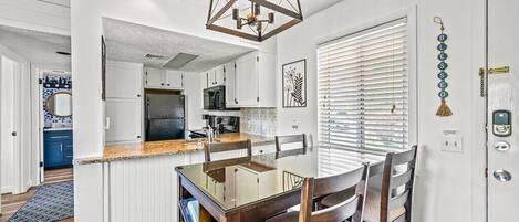 Una cocina moderna con armarios blancos, encimera de granito e iluminación colgante.