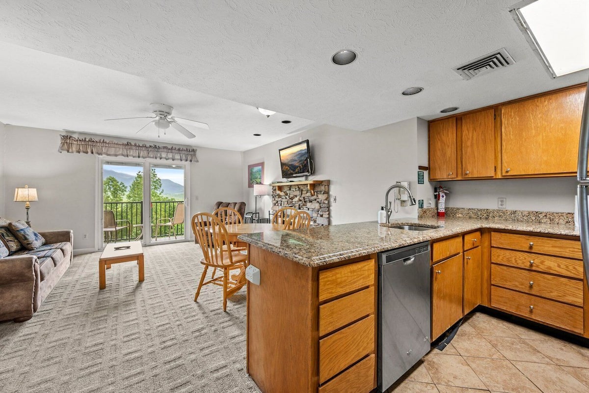 Eine geräumige Küche mit Holdekor-Schränken, einer Granit Arbeitsplatte und einem Geschirrspüler. Es gibt eine Essecke mit Tisch und Stühlen sowie ein Wohnzimmer mit Sofa und Lampe.