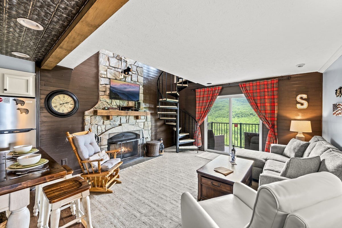 Ein gemütliches Wohnzimmer mit Kamin aus Stein, einem an der Wand befestigten Fernseher und einer komfortablen Sitzecke mit Sofa und Sesseln.