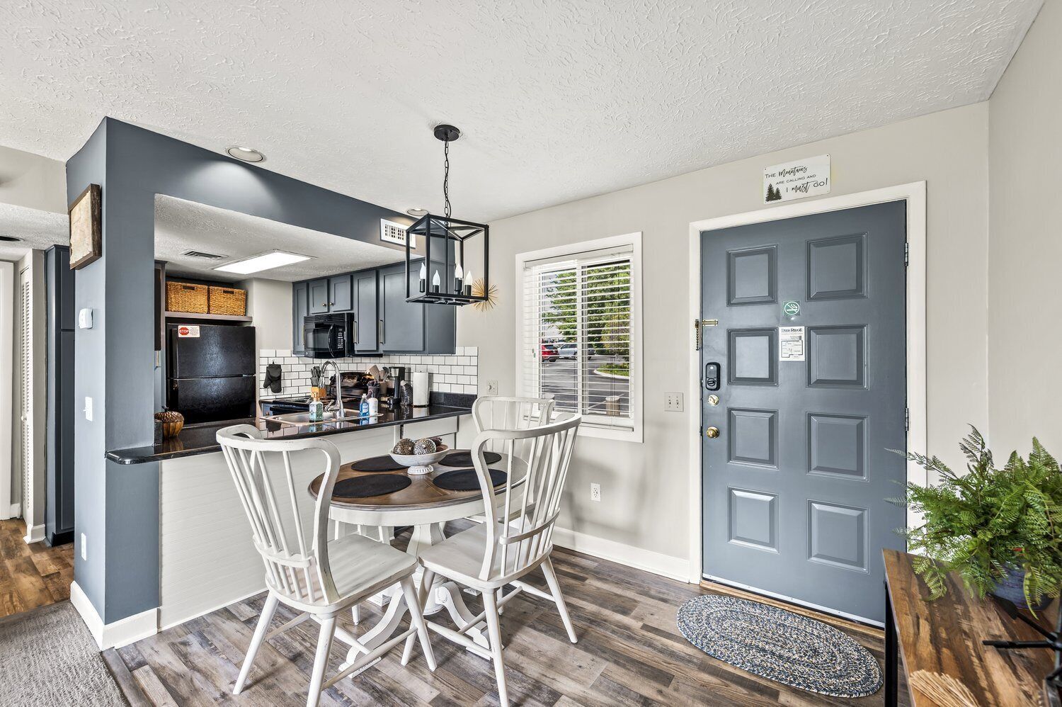 A modern kitchen with dark cabinetry, a central island, and a dining area with white chairs.