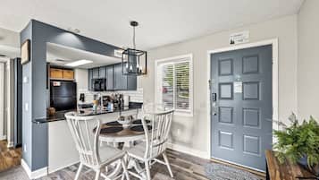 A modern kitchen with dark cabinetry, a central island, and a dining area with white chairs.