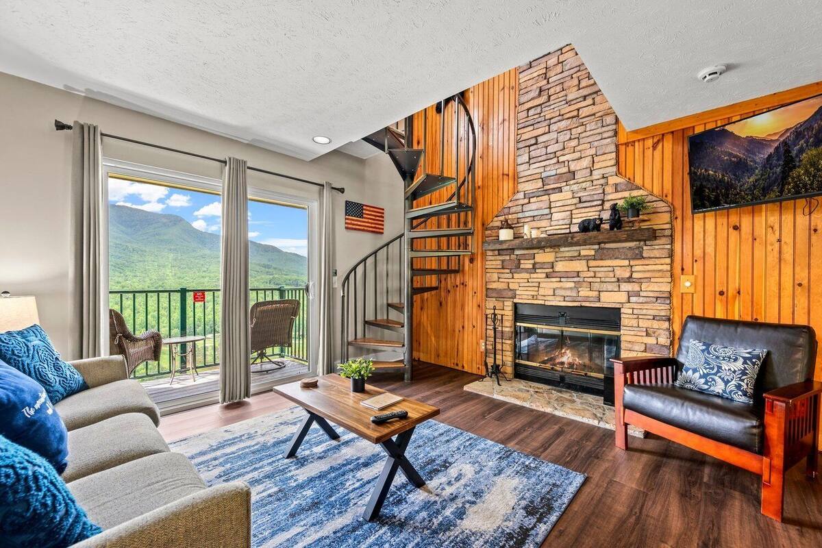 Ein geräumiges Wohnzimmer mit Kamin, ein Balkon mit Panoramablick auf die Berge und eine gemütliche Sitzecke.