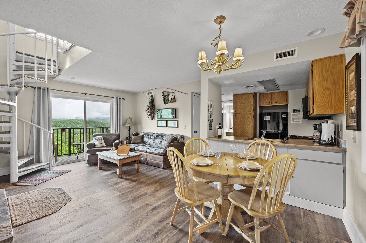 A spacious living area with a wooden dining table, a sofa, and a staircase leading to a balcony.