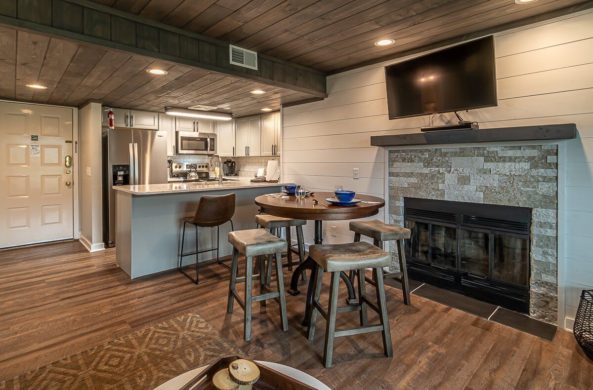 A modern kitchen with a central island, a dining area with stools, and a fireplace.