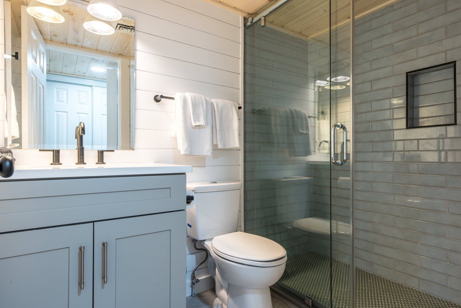 Un baño moderno con un tocador blanco, una cabina de ducha de vidrio y un inodoro.