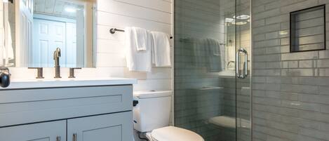 A modern bathroom with a white vanity, a glass shower enclosure, and a toilet.