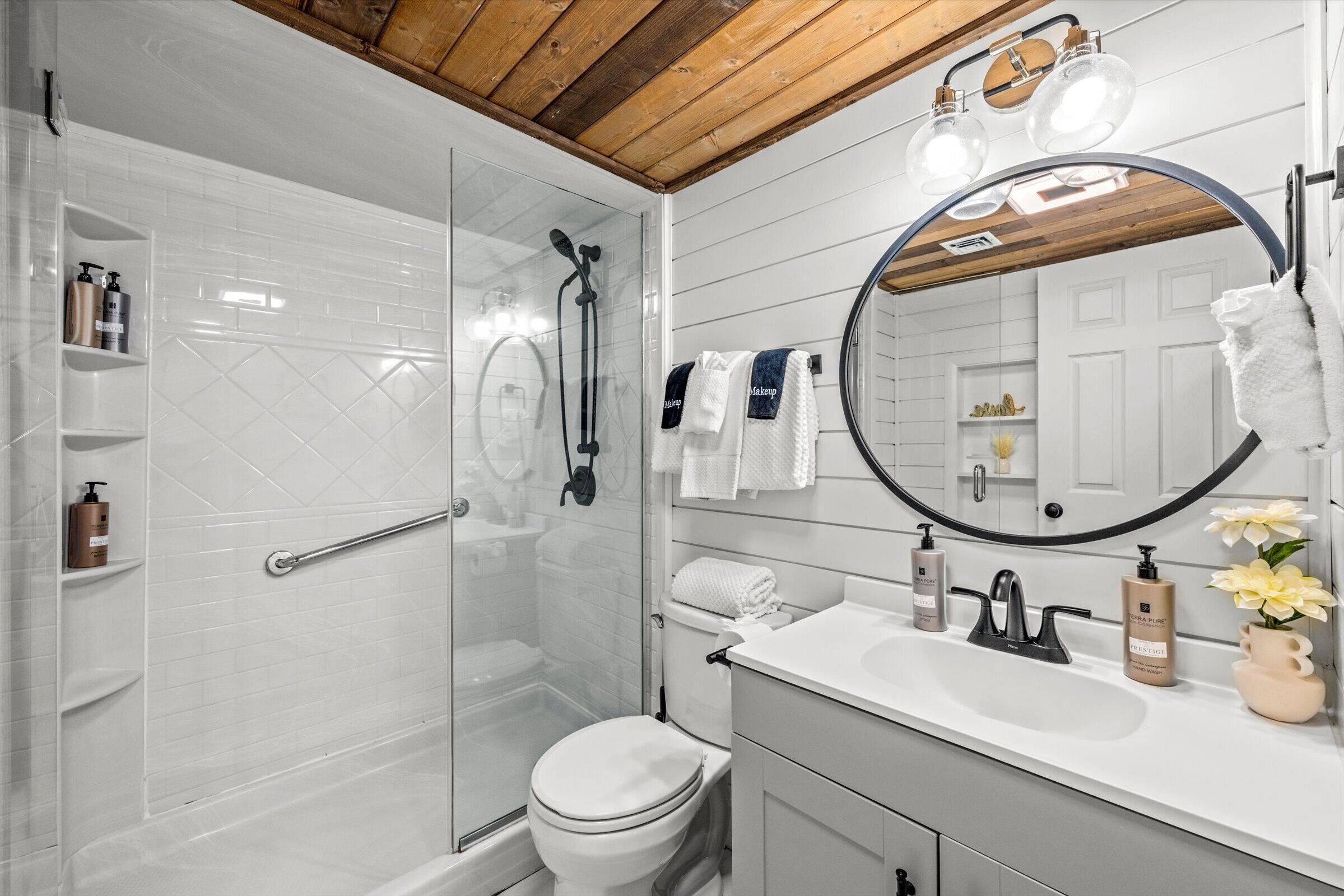 Une salle de bain moderne avec une douche à parois de verre, des toilettes blanches, un meuble-lavabo avec un miroir et un lavabo blanc.