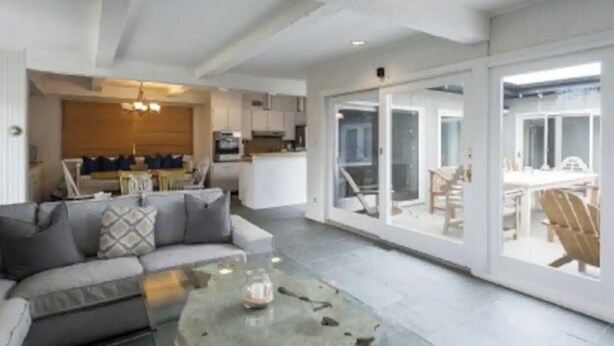 A spacious living area with a sofa, a glass coffee table, and a view of a kitchen and dining area through large sliding glass doors. - Cozy Hamptons Beach House 1 Block from the Beach!  (Montauk)