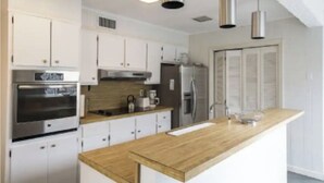 A modern kitchen with white cabinets, stainless steel appliances, a wooden countertop, and pendant lighting. - Cozy Hamptons Beach House 1 Block from the Beach!  (Montauk)
