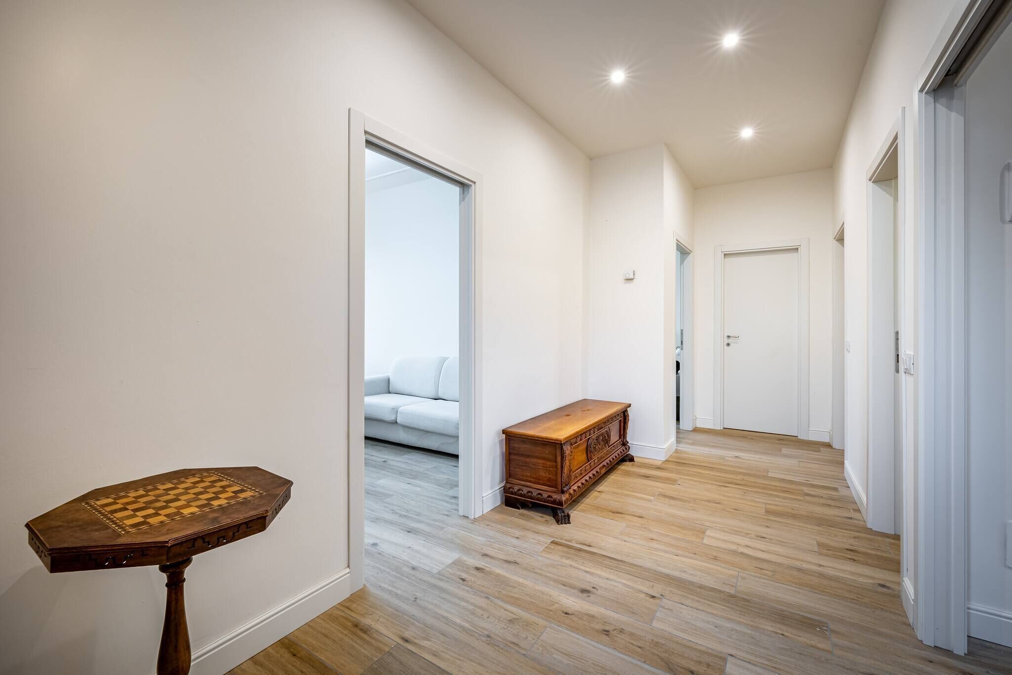 Um corredor com piso de madeira, uma mesa de xadrez e um baú de gavetas de madeira.