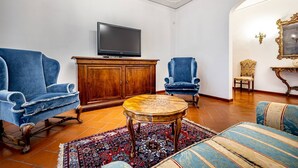Een woonkamer met een televisie, twee blauwe fauteuils, een houten salontafel en een vloerkleed met een patroon.