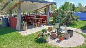 Un espace extérieur abrité, aménagé avec une table et des chaises, entouré de plantes en pot et d’un mur de pierre.