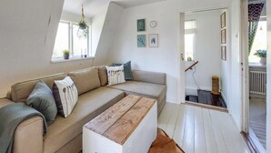 Un salon chaleureux avec un canapé, une commode en bois et un miroir qui reflète un escalier.