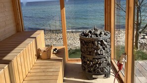 Eine Holzsauna mit Meerblick, einem Feuerkorb und einer hölzernen Sitzbank.