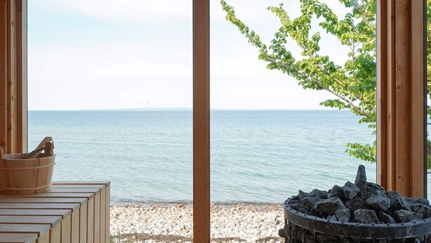 Eine Holzterrasse mit Blick aufs Meer, ein Holzeimer und eine Feuerstelle aus Stein.