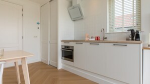 A modern kitchen with white cabinets, a wooden countertop, a built-in oven, and a window with blinds. - Charming Holiday Home With a Terrace (Zoutelande)