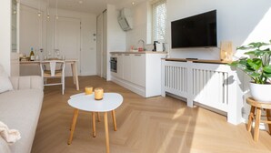 A modern living room with a sofa, a round white table, and a TV mounted on the wall. - Charming Holiday Home With a Terrace (Zoutelande)