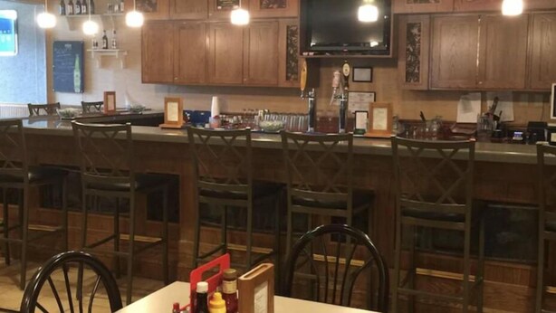 Interior de restaurante con mostradores de madera, luces colgantes y un televisor montado en la pared.