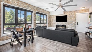 A modern living room with a large gray sectional sofa, a dining table with chairs, and a fireplace.