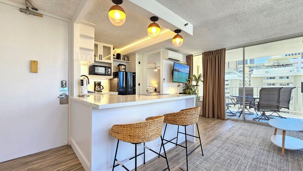 Une cuisine moderne avec un coin bar, un téléviseur à écran plat et un balcon aménagé avec du mobilier d’extérieur.