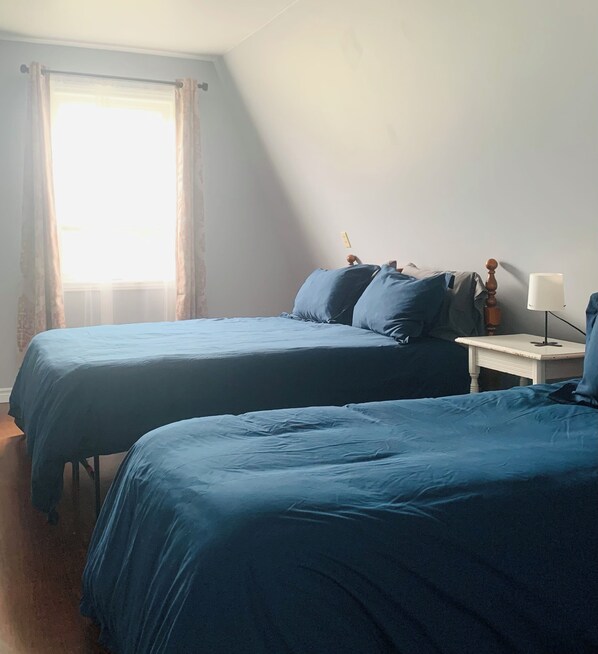Une chambre avec deux lits, une petite table avec une lampe et une fenêtre avec des rideaux.