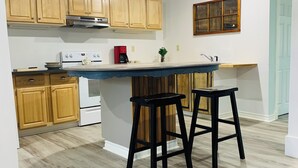 Une cuisine moderne avec des meubles en bois, un îlot central doté de tabourets, un four encastré et une fenêtre au-dessus de l’évier.