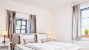 Ein Schlafzimmer mit einem Bett, zwei Nachttischen, einem Fenster mit Vorhängen und einer kleinen Pflanze auf der Fensterbank.
