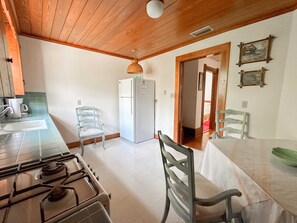 Una cocina con estufa a gas, refrigerador y una mesa de comedor con sillas.
