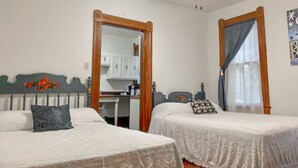 Un dormitorio con dos camas, un ventilador de techo y vista a una cocina a través de una puerta abierta.