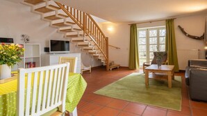 A living room with a wooden staircase, a dining area with a table and chairs, a sofa, and a TV on a white cabinet. - Comfy Apartment With Terrace (Dranske)