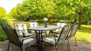 A round metal table with a glass vase of flowers, surrounded by six chairs with checkered cushions. - Comfy Apartment With Terrace (Dranske)