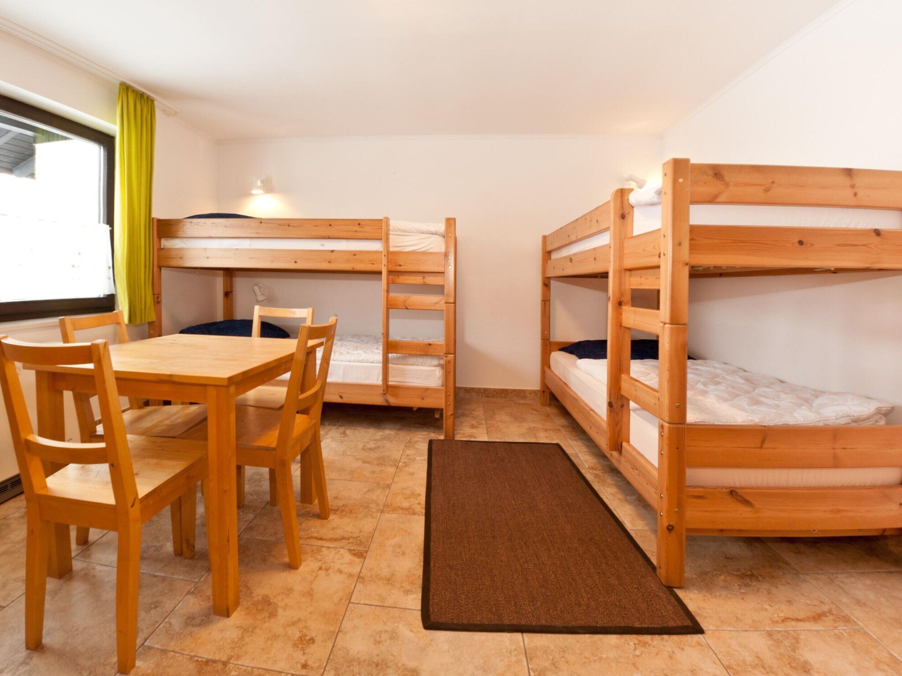 Un dormitorio con literas, una mesa de madera, sillas y una alfombra.