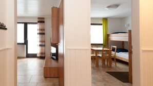 Una habitación moderna y luminosa con un mueble bajo de madera para televisión, una mesa de comedor con sillas y una cama litera.