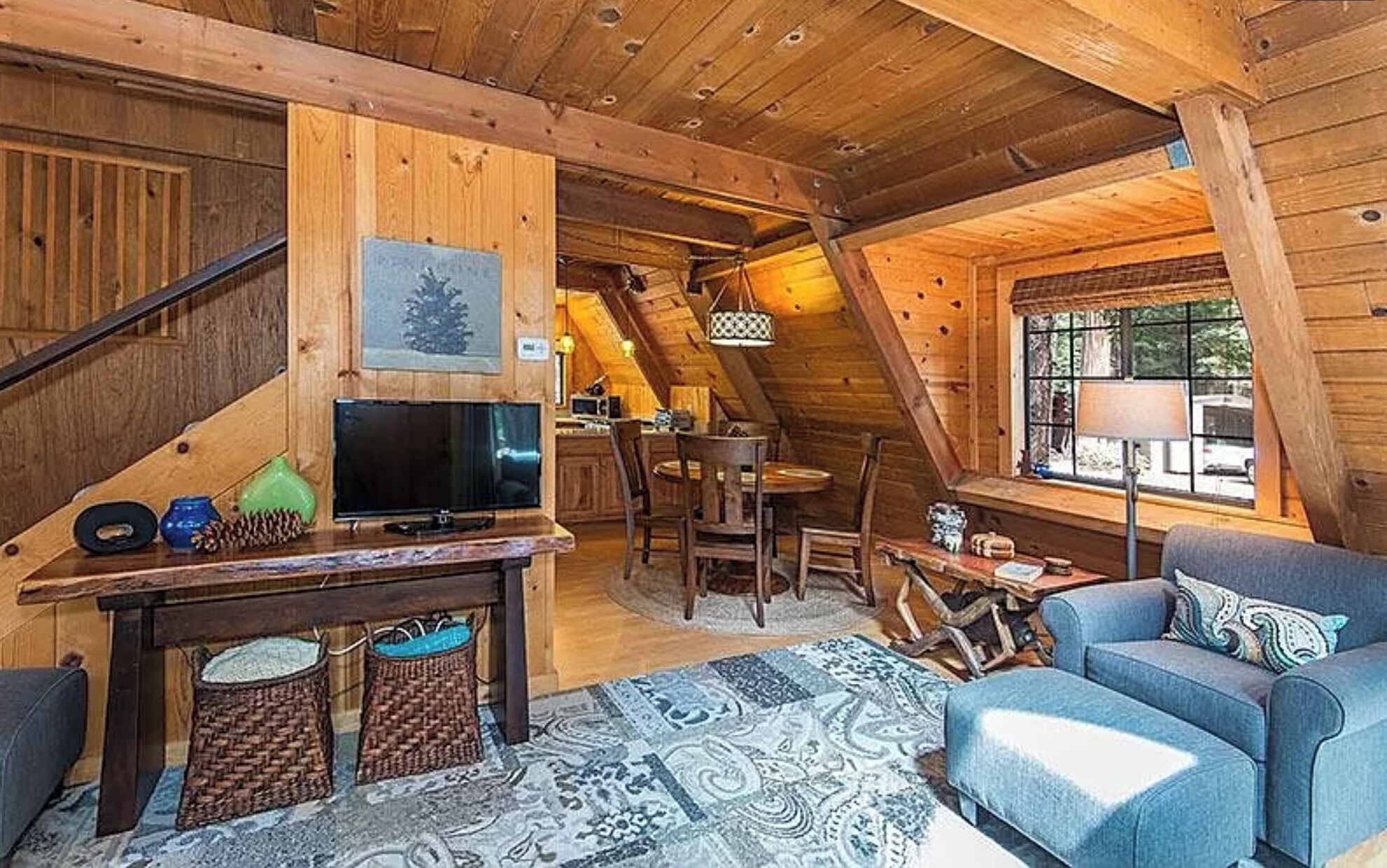 A cozy cabin interior with a wooden ceiling, a TV on a wooden table, a sofa, and a dining area.