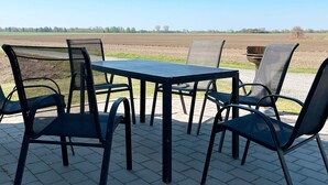 An outdoor patio with a table and chairs, a view of a plowed field, and a clear sky. - 4 Star Holiday Home in Skivarp (Skivarp)