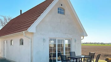 A single-story building with a sloped roof, a large sliding glass door, and a patio with a table and chairs.