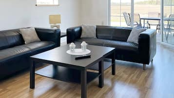 A modern living room with two black leather sofas, a dark wooden coffee table, and a view of a field through large windows.
