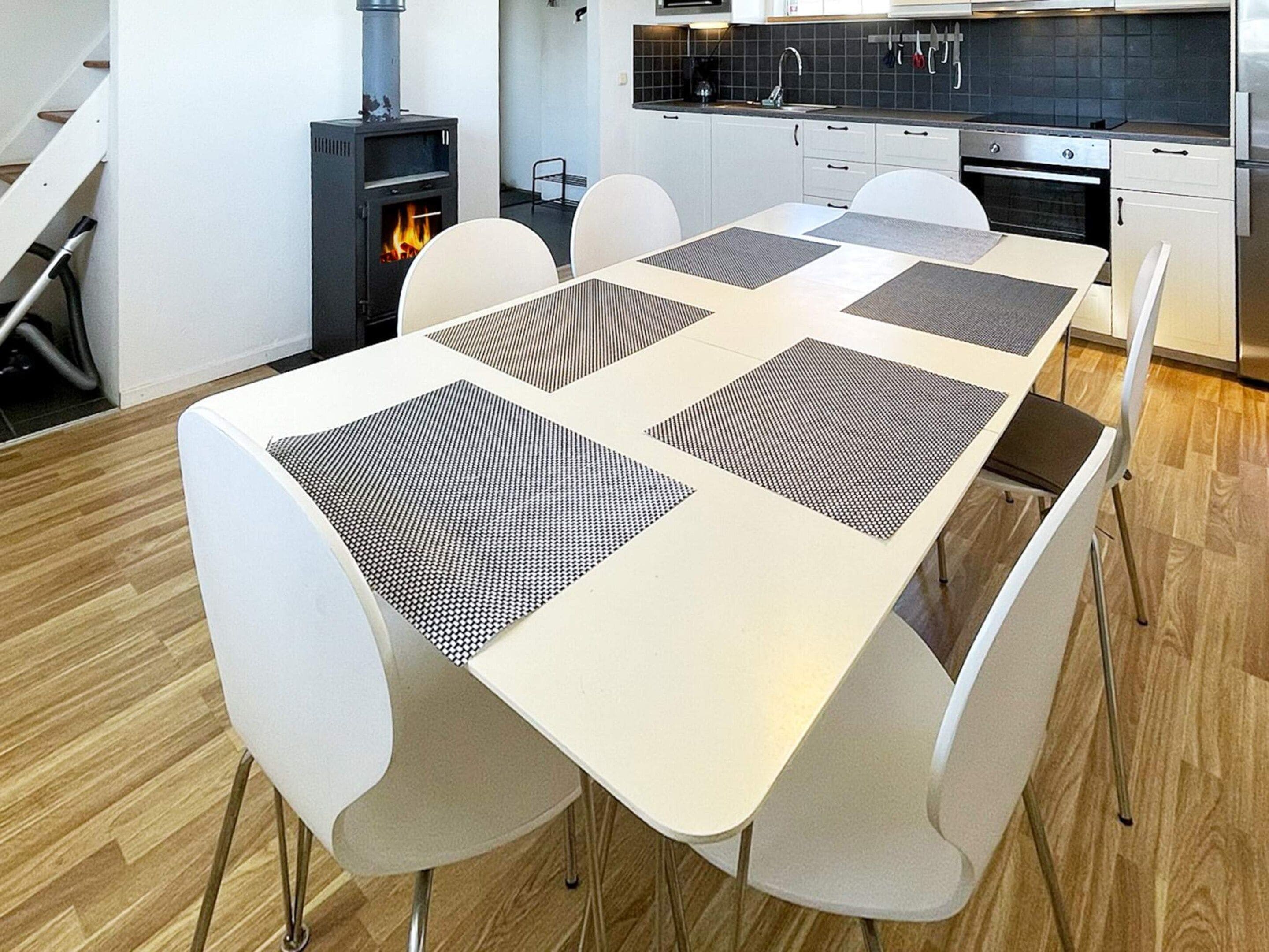 A modern kitchen with white cabinetry, a built-in stove, and a dining area with a white table and chairs.